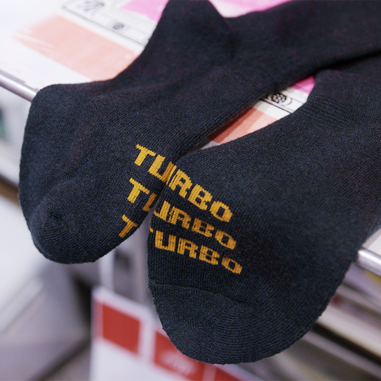 A pair of black crew socks with 'TURBO' printed in yellow across the toes, resting on a store shelf.